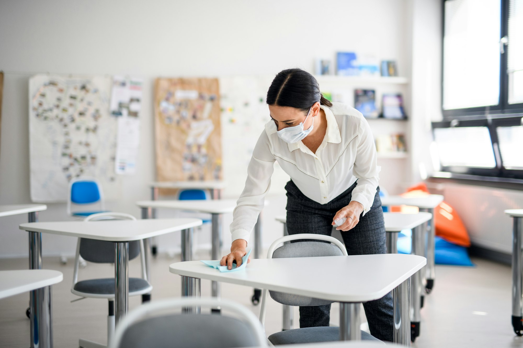 Teacher back at school after covid-19 quarantine and lockdown, disinfecting desks