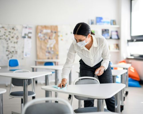 Teacher back at school after covid-19 quarantine and lockdown, disinfecting desks