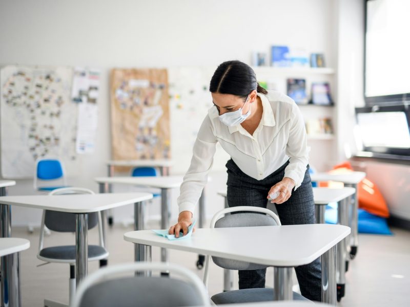 Teacher back at school after covid-19 quarantine and lockdown, disinfecting desks